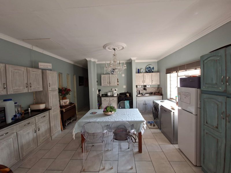 Spacious open-plan kitchen and dining area featuring light-toned built-in cabinetry, granite countertops, tiled flooring, and a decorative ceiling rose with chandelier.