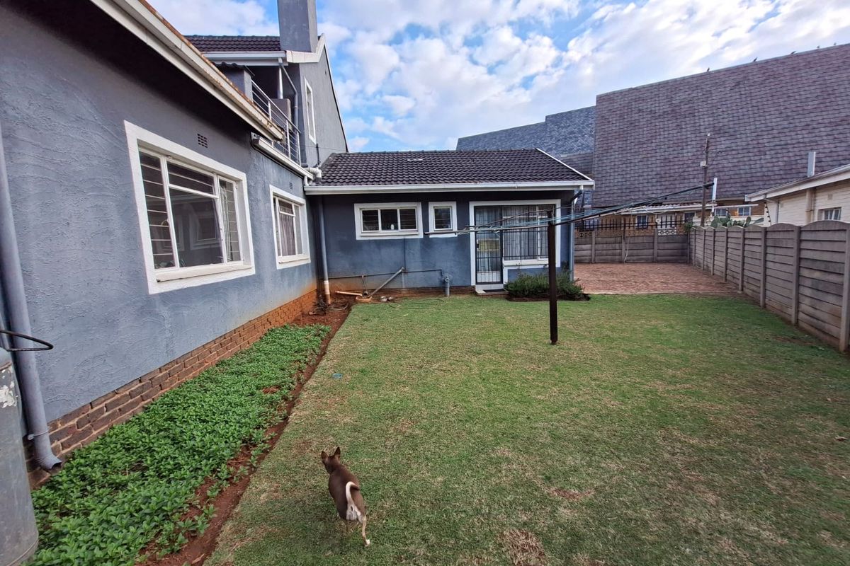 Rear view of the property featuring a lawn, paved section, concrete boundary wall, and tiled roof structure.