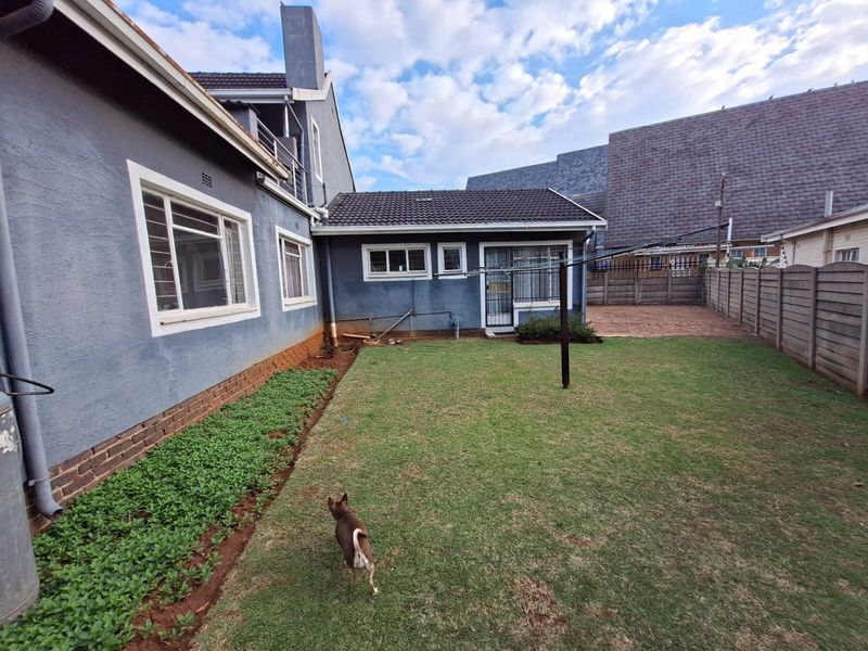 Rear view of the property featuring a lawn, paved section, concrete boundary wall, and tiled roof structure.