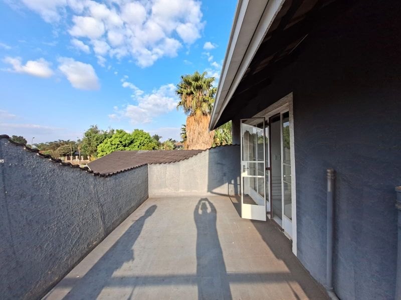 An open-air balcony featuring a plastered boundary wall and direct access to the interior through a glass sliding door.