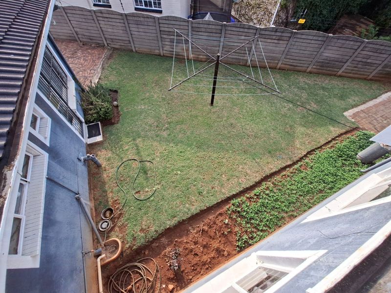An elevated view of the rear garden featuring a lawn area, paved sections, and a precast concrete boundary wall.