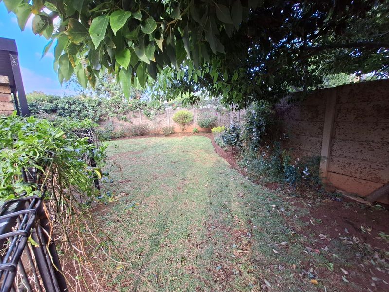 A private backyard garden featuring a lawn area enclosed by a precast concrete boundary wall and mature trees.