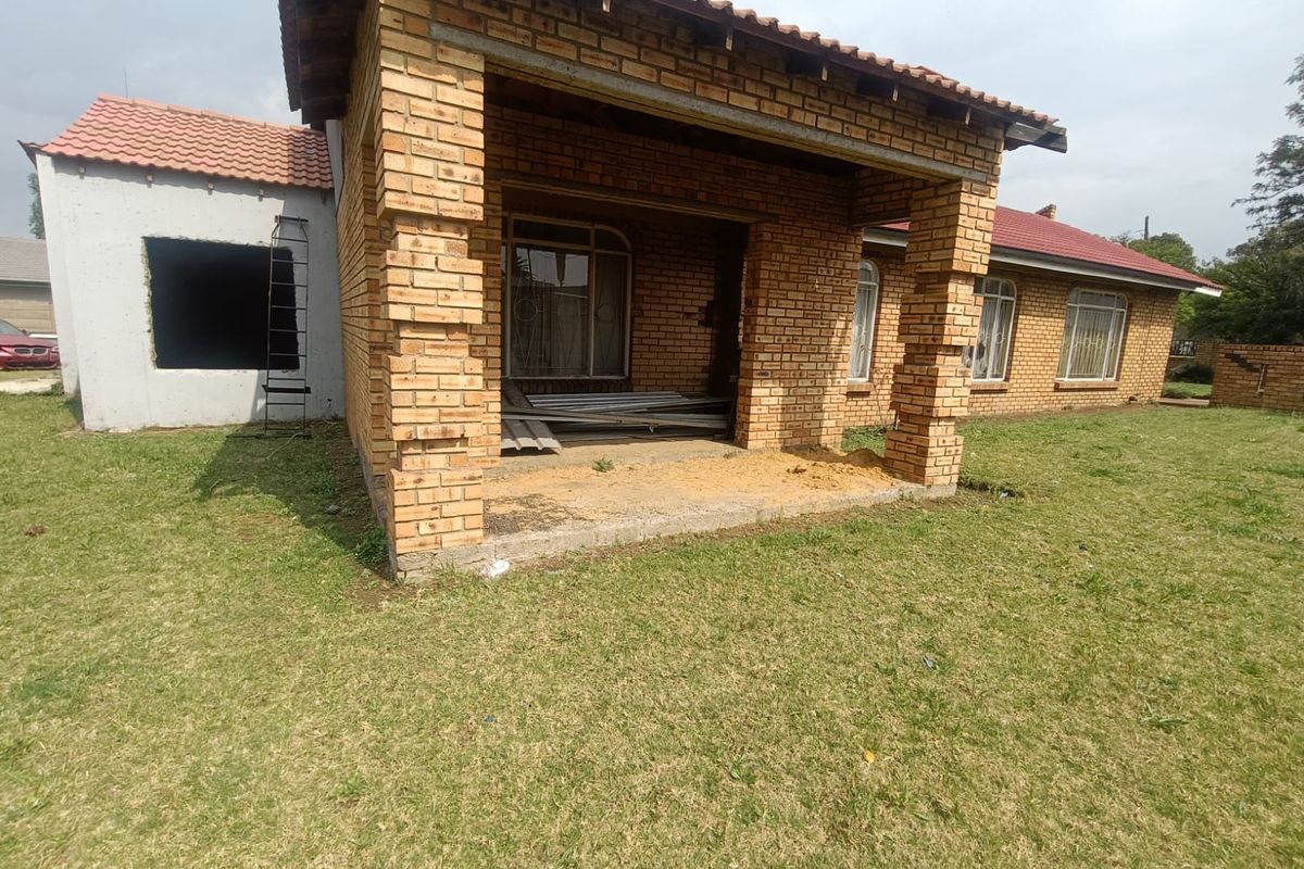 Rear view of a house showing an unfinished patio area, exposed brickwork, and a missing window frame, indicating ongoing construction or renovation work.