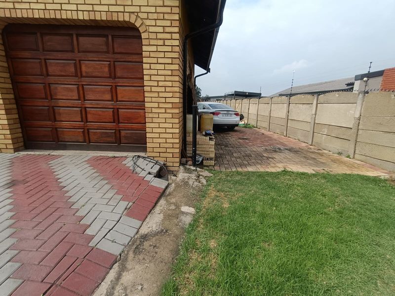 Exterior view of a brick garage with a wooden door, featuring a paved driveway and a precast concrete boundary wall.