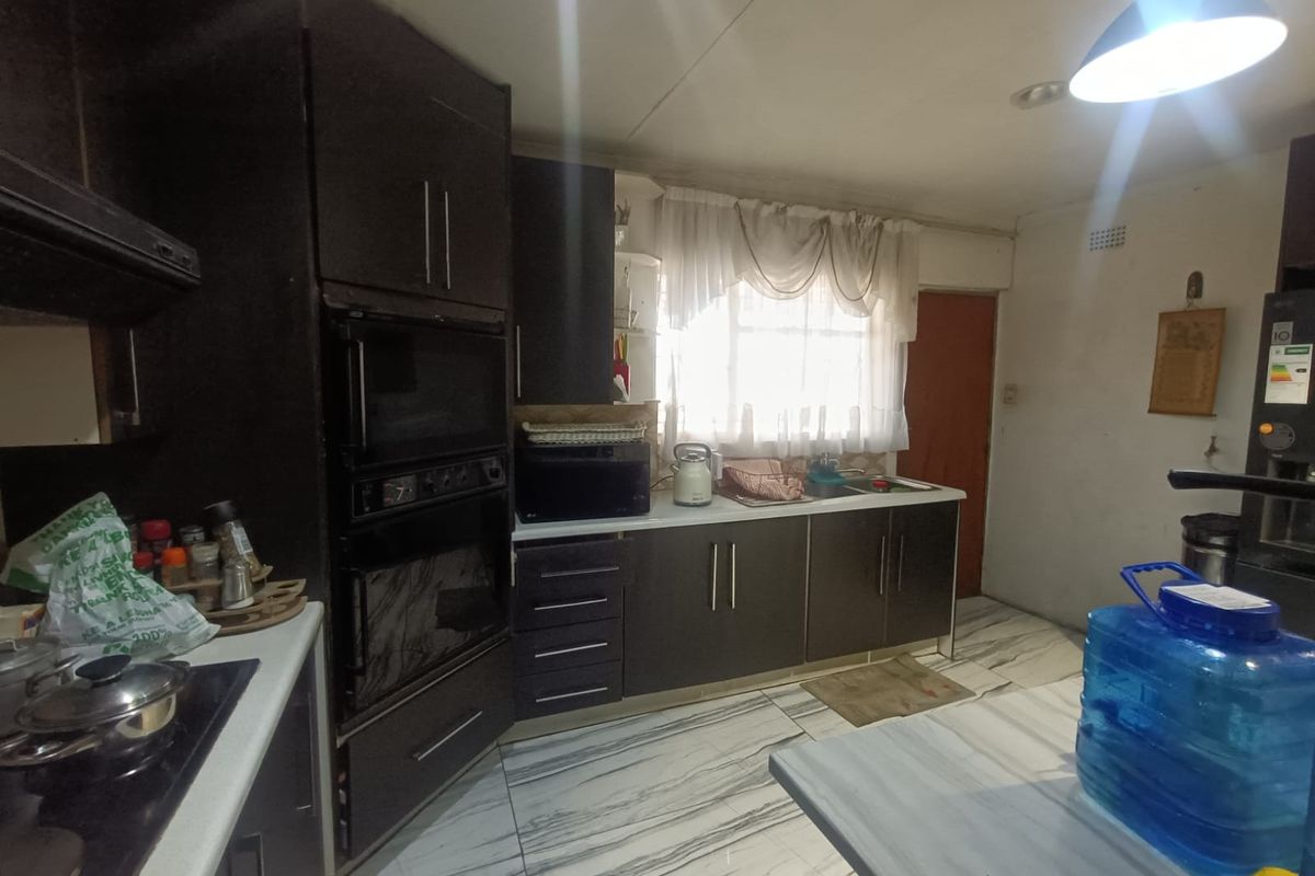 A functional kitchen featuring dark built-in cabinetry, integrated oven, hob, and tiled flooring, offering a practical layout for daily meal preparation.