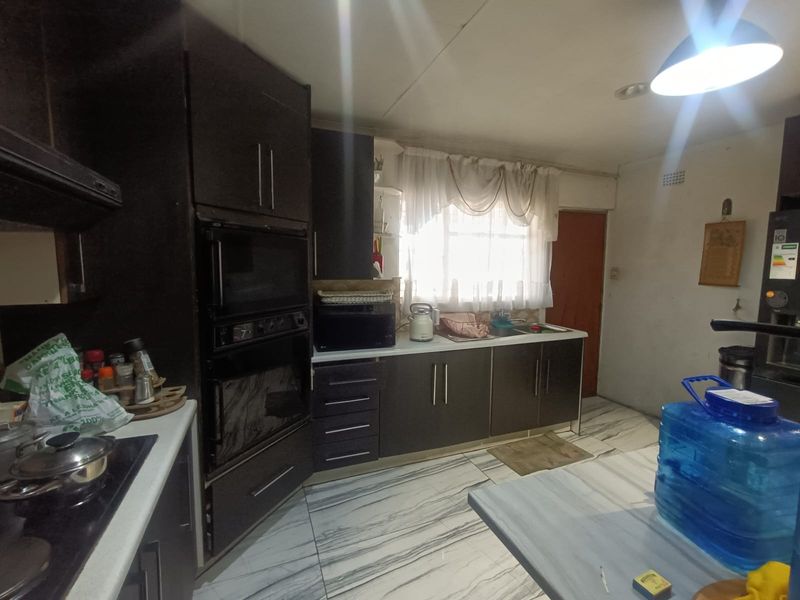 A functional kitchen featuring dark built-in cabinetry, integrated oven, hob, and tiled flooring, offering a practical layout for daily meal preparation.