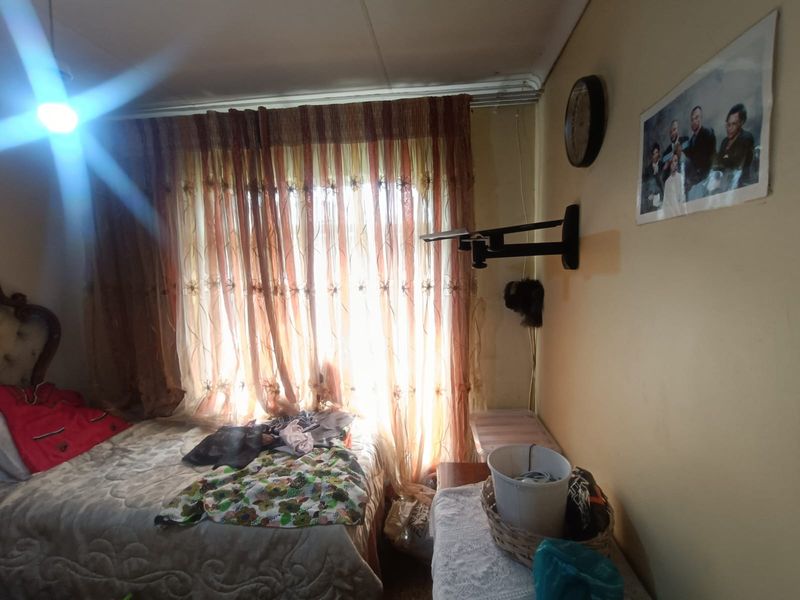 A bedroom featuring a wall-mounted television bracket and window with curtains, requiring cosmetic updates to improve the overall aesthetic and condition.
