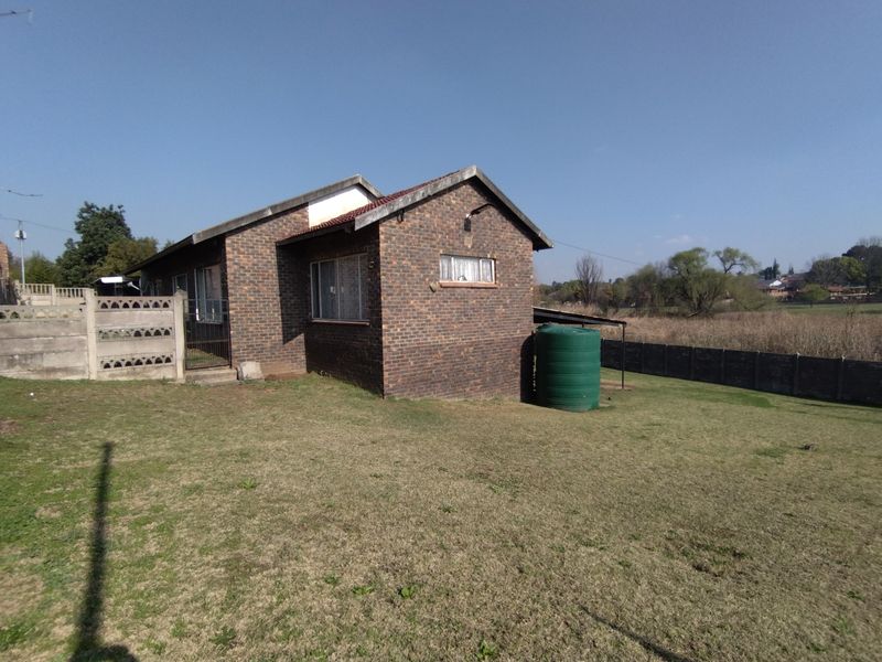 Rear view of a face brick house featuring a tiled roof, a water storage tank, and a large garden enclosed by precast concrete walls.