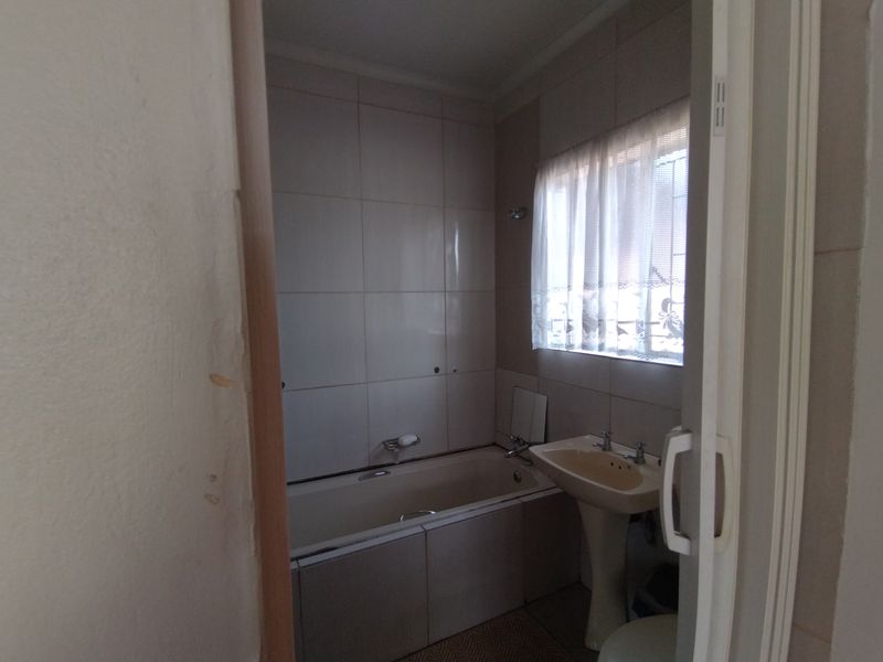 A functional bathroom featuring a bathtub, pedestal basin, and tiled walls, offering a clean canvas for potential modern updates.