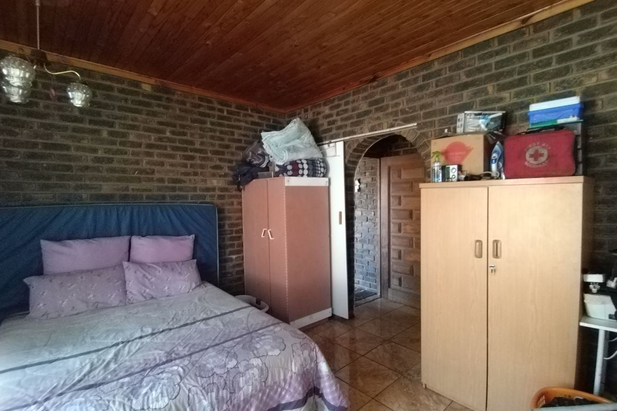 A bedroom featuring exposed brick walls, a timber ceiling, and tiled flooring, accessible through an arched doorway.