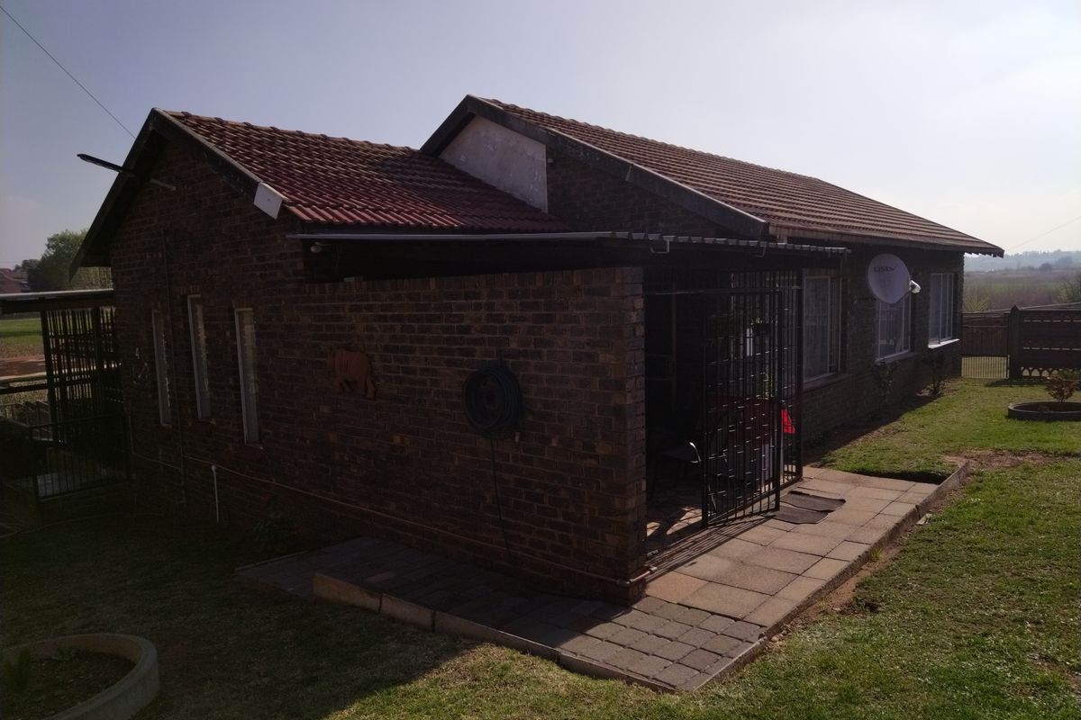 Rear view of a face brick house featuring a tiled roof, paved patio area, and security gate access.