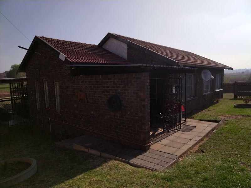 Rear view of a face brick house featuring a tiled roof, paved patio area, and security gate access.