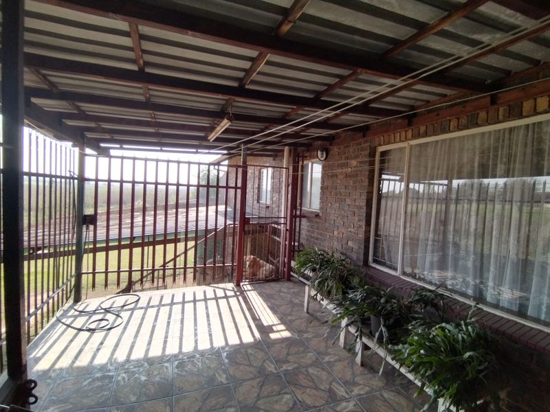 A covered outdoor patio area featuring tiled flooring, exposed brickwork, and a metal security gate, providing a functional space for outdoor relaxation.