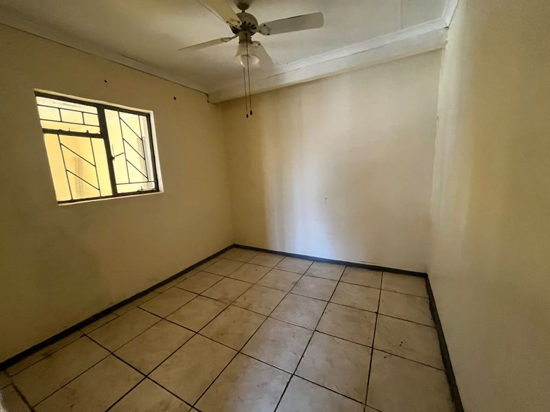 An empty bedroom featuring tiled flooring, a ceiling fan, and security bars on the window, requiring cosmetic updates to improve its overall condition.