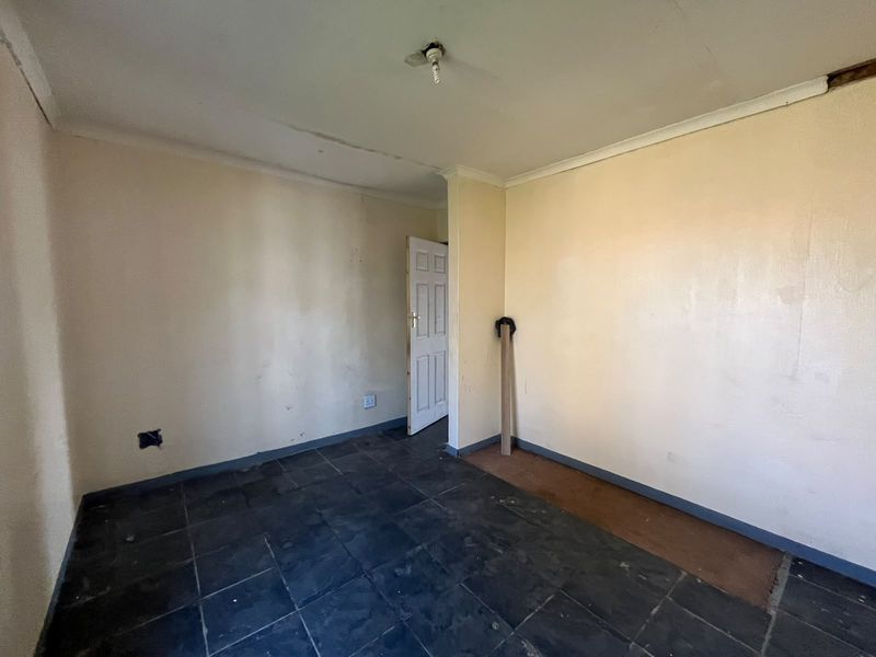 An empty bedroom featuring dark tiled flooring and plain walls, requiring cosmetic updates and minor repairs to electrical and ceiling fixtures.