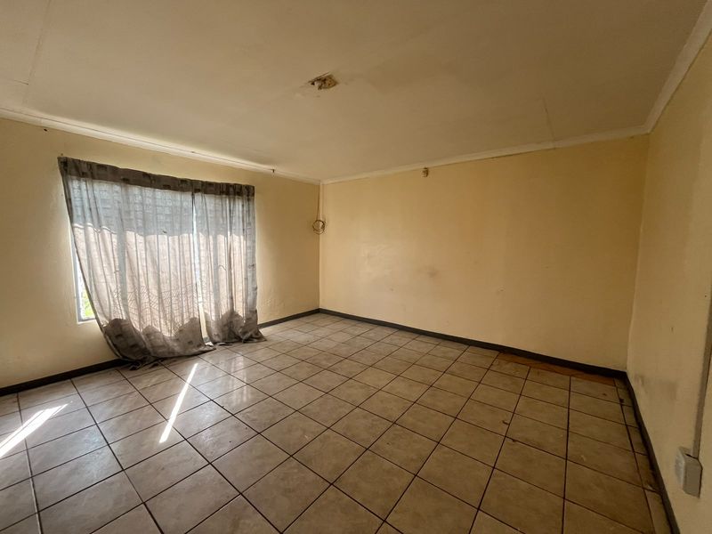 An empty living room featuring tiled flooring and a sliding glass door, requiring cosmetic updates and minor electrical repairs.