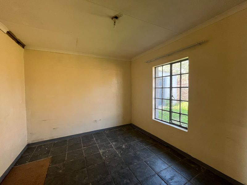 An empty bedroom featuring dark ceramic floor tiles, a steel-framed window, and plain walls, offering a blank canvas for renovation or interior design updates.