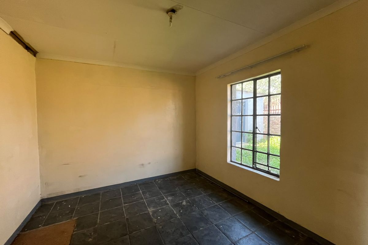 An empty bedroom featuring dark ceramic floor tiles, a steel-framed window, and plain walls, offering a blank canvas for renovation or interior design updates.