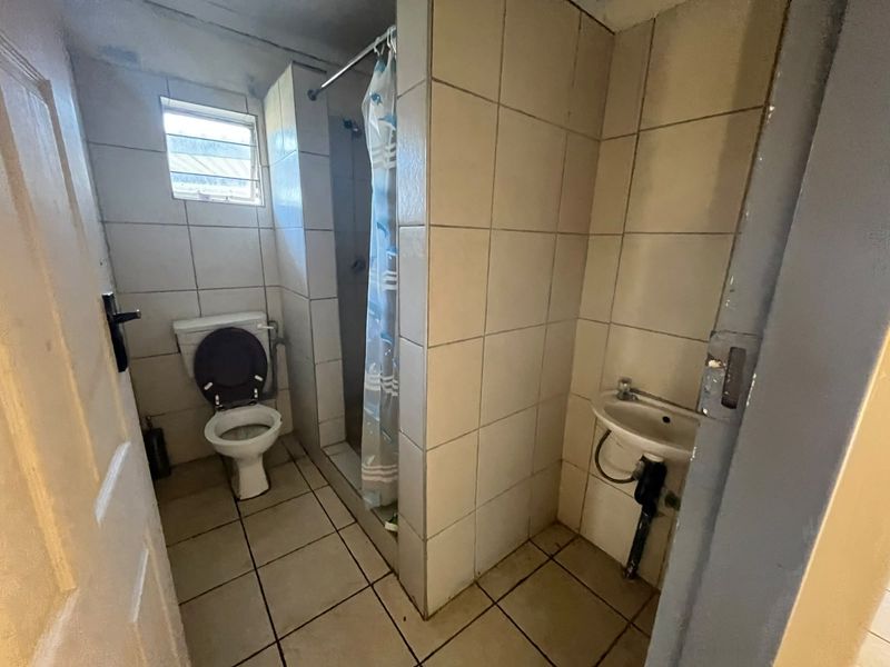 A functional bathroom featuring tiled walls and floors, a shower enclosure, a standard toilet, and a wall-mounted basin.