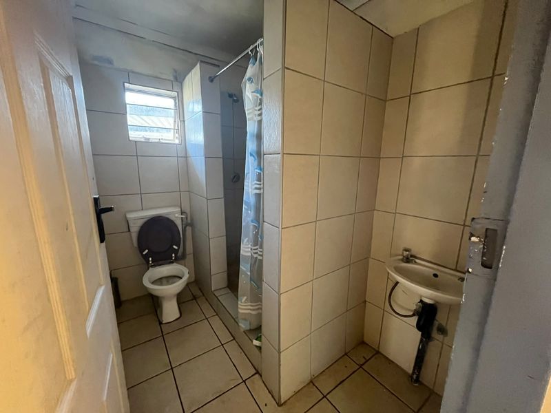 A functional bathroom featuring a shower, toilet, and wall-mounted basin with tiled finishes, currently requiring cosmetic updates and maintenance.