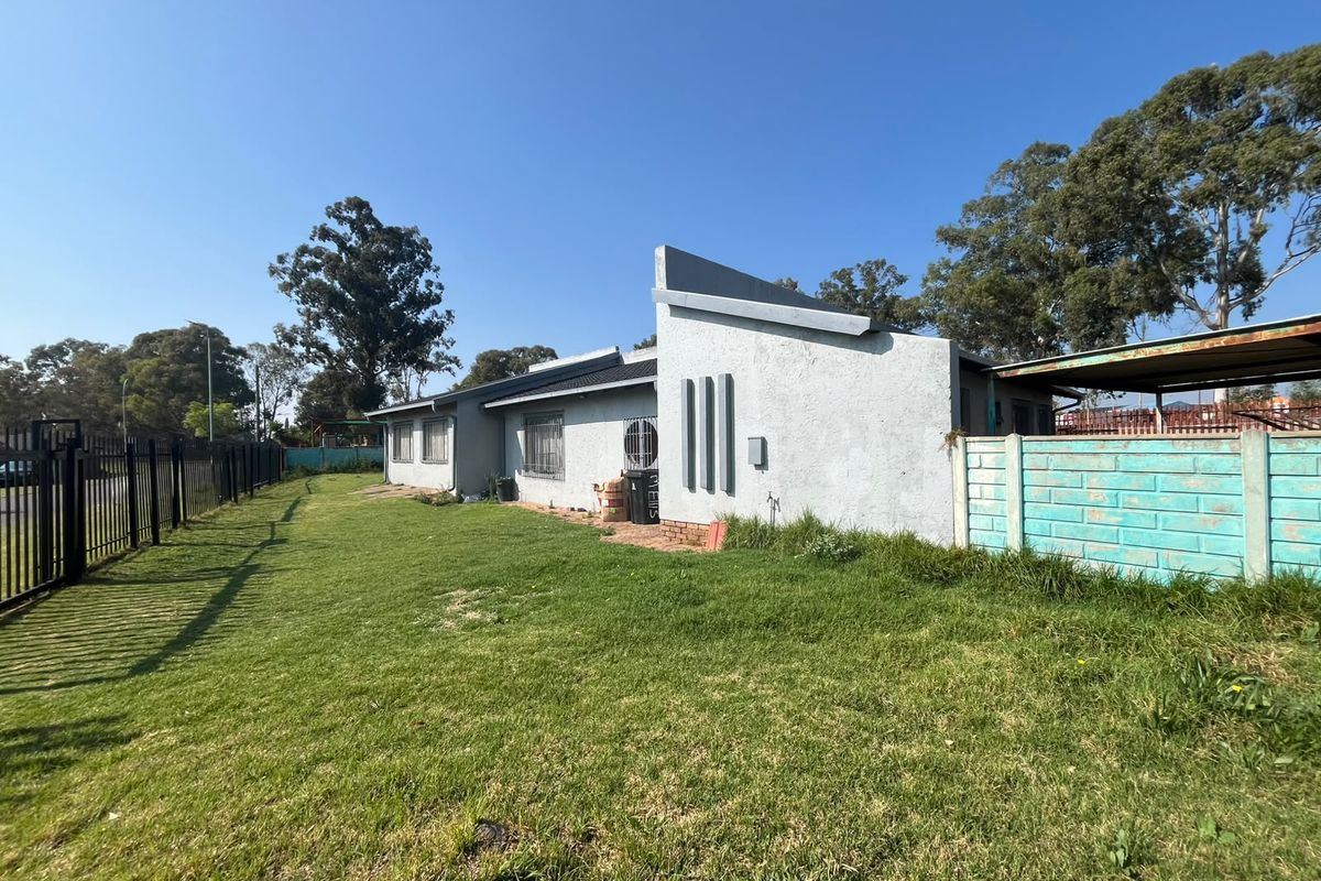 Rear view of the property featuring a large lawn, metal security fencing, and a concrete boundary wall with visible exterior wall finishes.