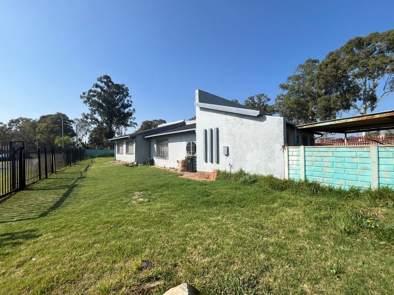 Rear view of the property featuring a large lawn, metal security fencing, and a concrete boundary wall with visible exterior wall finishes.