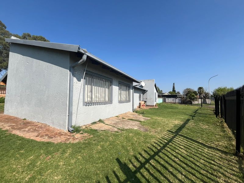 Rear exterior view of the property featuring a grass lawn, paved walkway, and metal perimeter fencing with security bars on the windows.