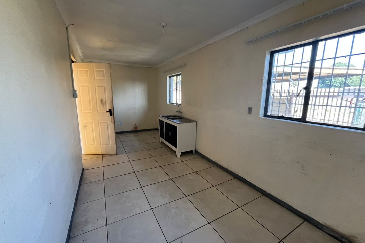 A basic, empty kitchen area featuring tiled flooring, a small sink unit, and security bars on the windows, requiring cosmetic updates.