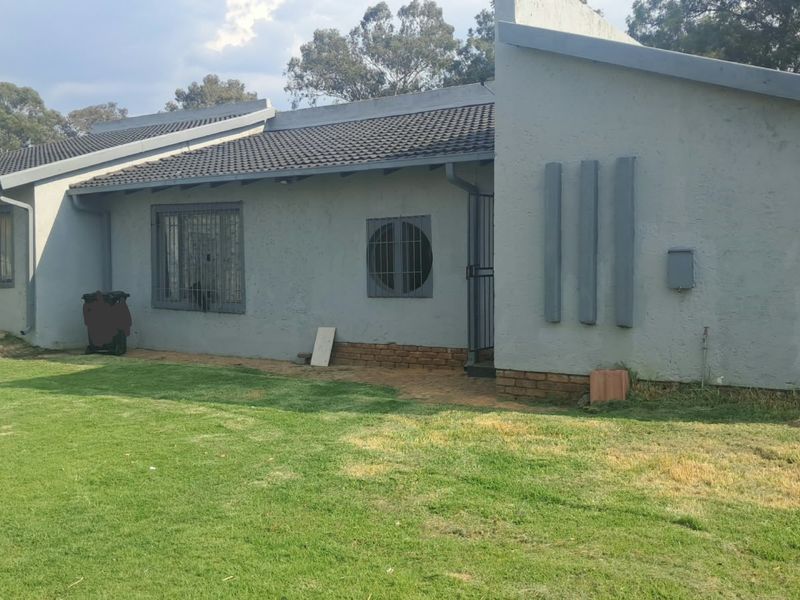 Rear view of the house featuring a tiled roof, plastered exterior walls with security bars on windows, and a surrounding lawn area.