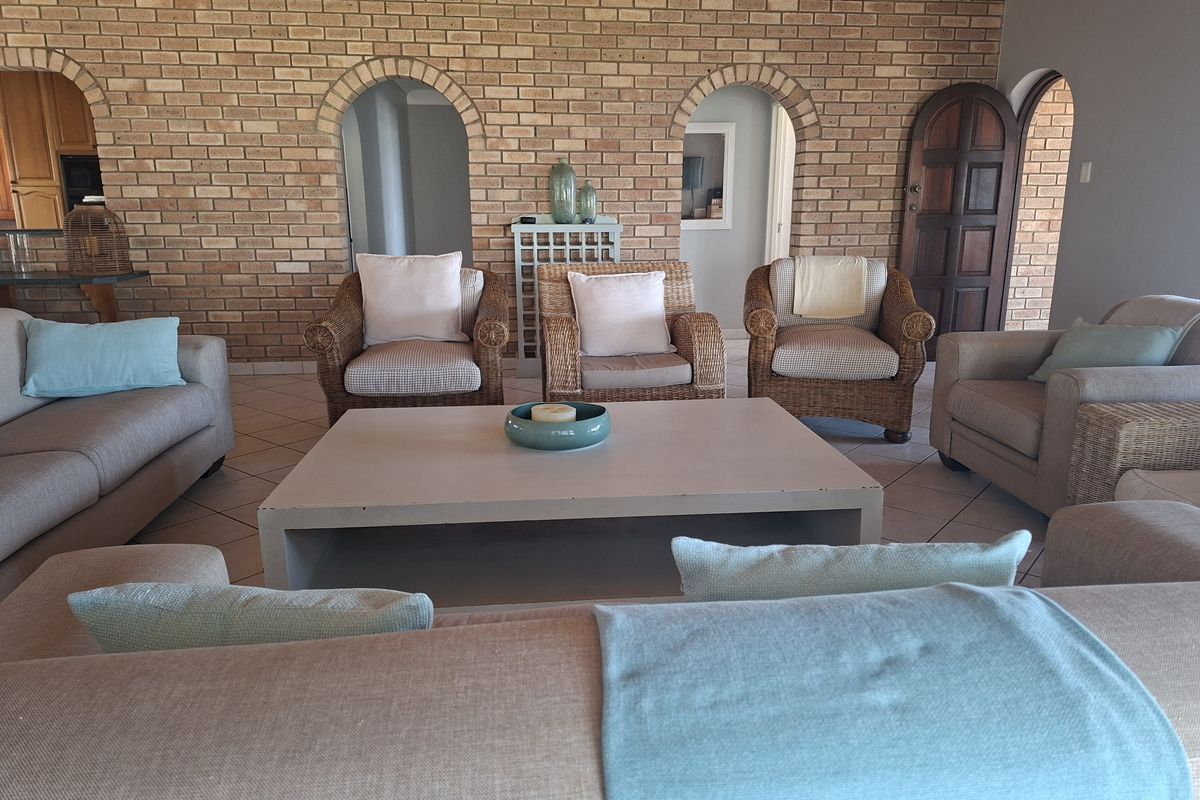 Spacious living room featuring a prominent exposed brick wall, arched architectural details, and a warm timber ceiling with neutral floor tiling.