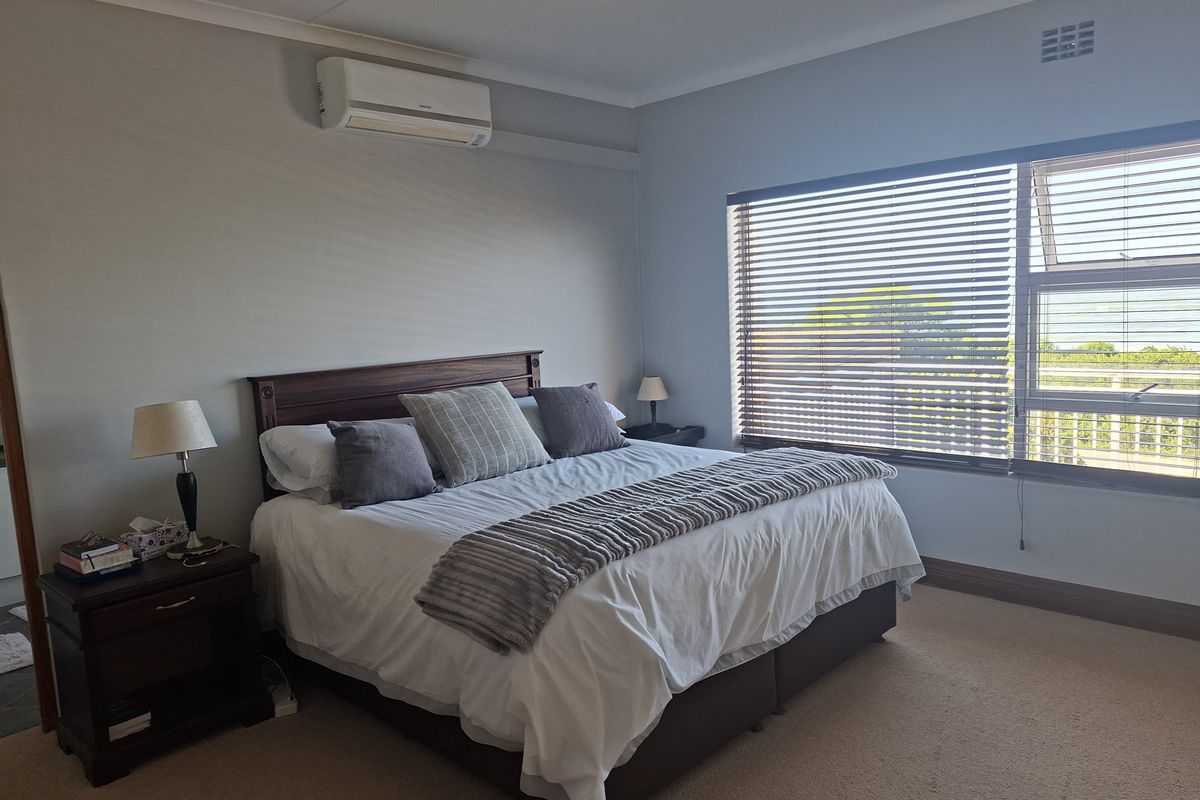 A well-maintained bedroom featuring carpeted flooring, a wall-mounted split-system air conditioner, and large windows with venetian blinds providing natural light.
