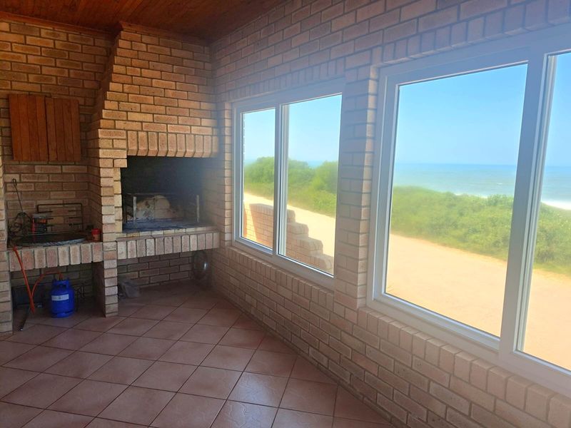 Enclosed patio area featuring a built-in brick braai, tiled flooring, and expansive windows offering scenic coastal views.