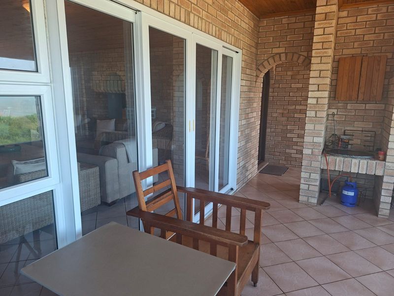 Covered patio featuring a built-in brick braai, tiled flooring, and large sliding glass doors providing seamless access to the interior living space.