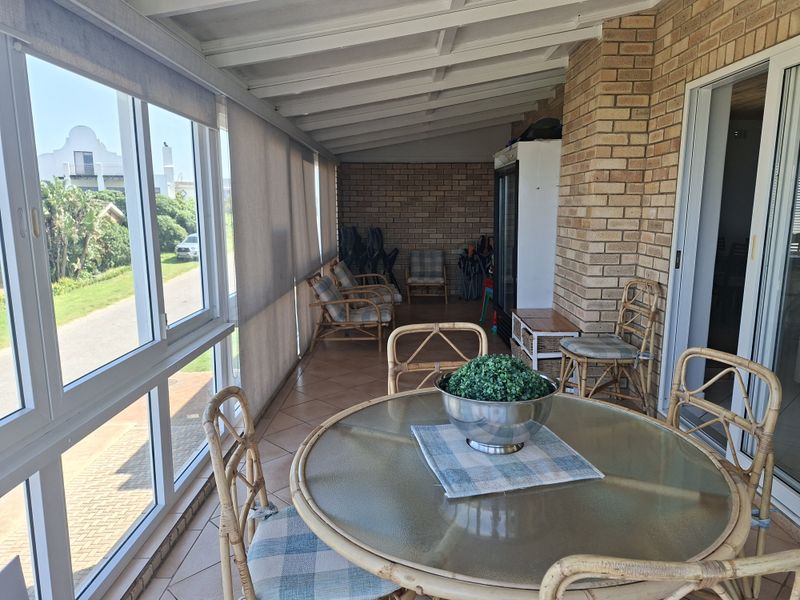 A covered patio area featuring exposed beam ceilings, brick walls, and tiled flooring, offering a bright space with large windows and sliding door access.