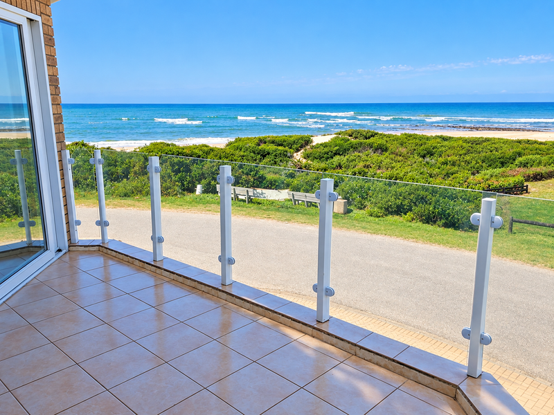 A clean, tiled balcony featuring a modern glass balustrade with unobstructed views of the ocean and coastal landscape.