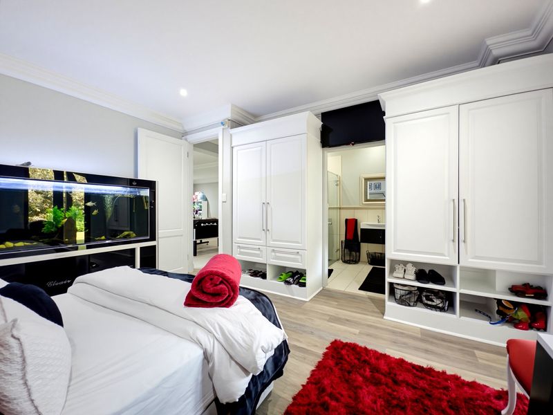 Spacious bedroom featuring extensive built-in cabinetry, modern laminate flooring, and direct access to an en-suite bathroom with recessed lighting and elegant coved cornicing.