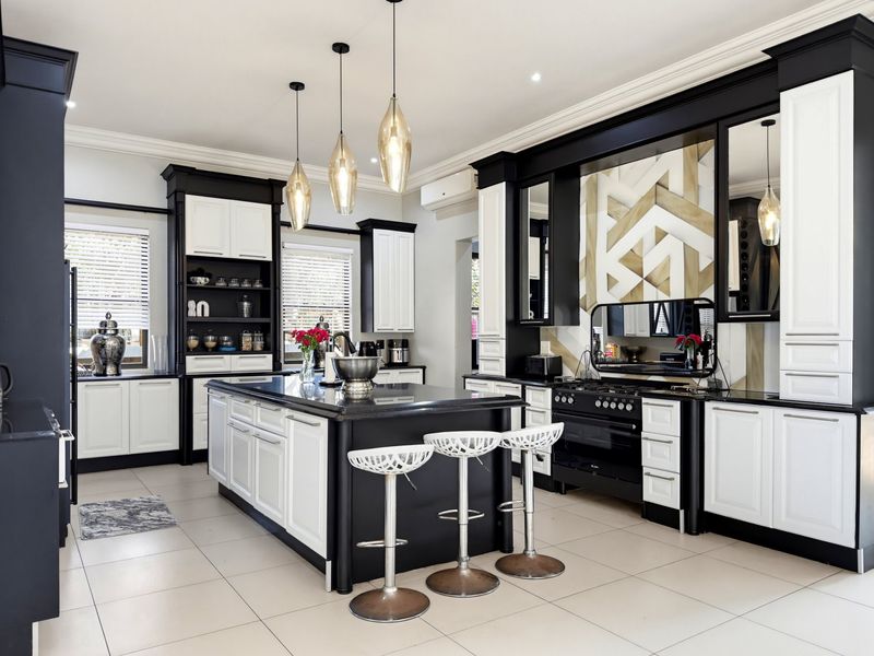 Modern kitchen featuring a central island, high-contrast cabinetry, professional-grade gas range, and elegant pendant lighting, finished with tiled flooring and decorative coving.