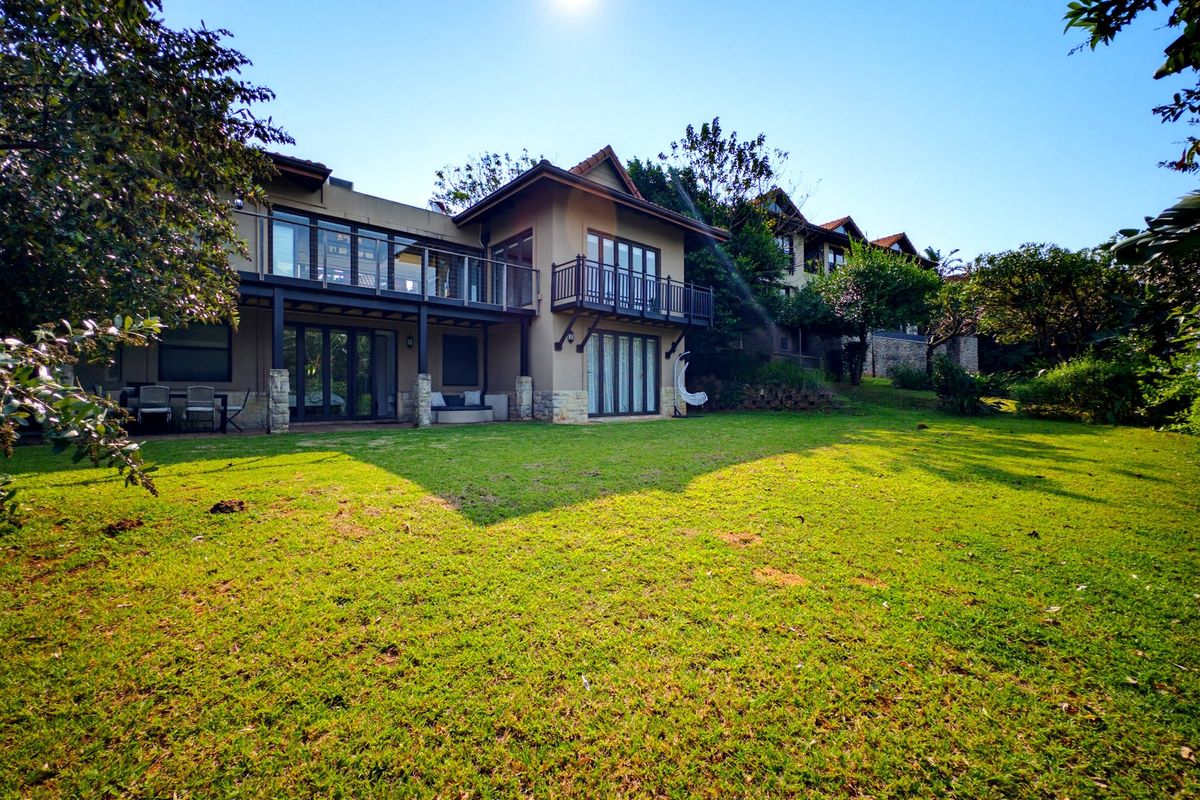 Rear view of a multi-story house featuring a spacious lawn, covered patio, and upper-level balconies with glass railings.