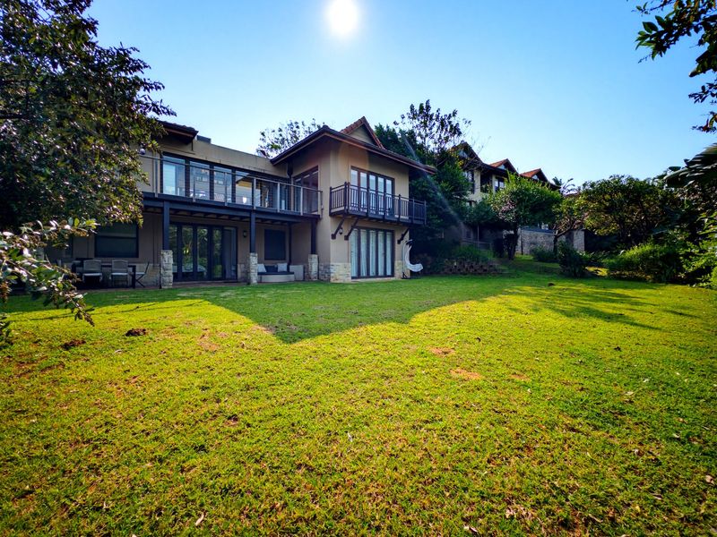 Rear view of a multi-story house featuring a spacious lawn, covered patio, and upper-level balconies with glass railings.
