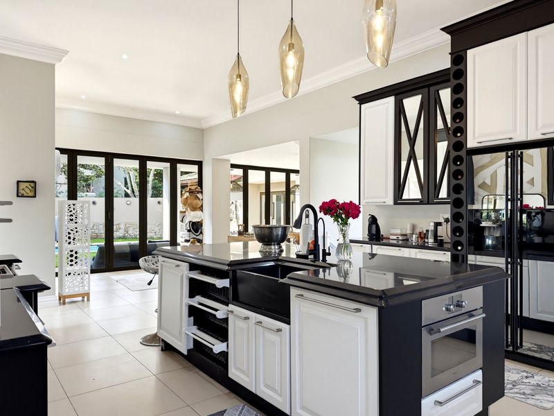 Modern kitchen featuring a large central island with a farmhouse sink, built-in oven, wine storage, and elegant pendant lighting, opening to an outdoor patio area.