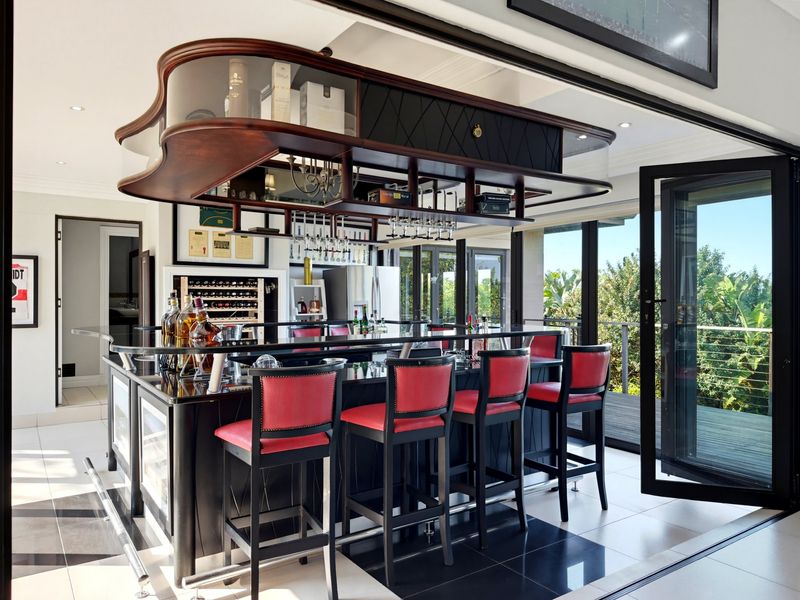 A sophisticated indoor bar area featuring a custom built-in counter, overhead glass storage, and seamless access to an outdoor deck through bi-fold doors.