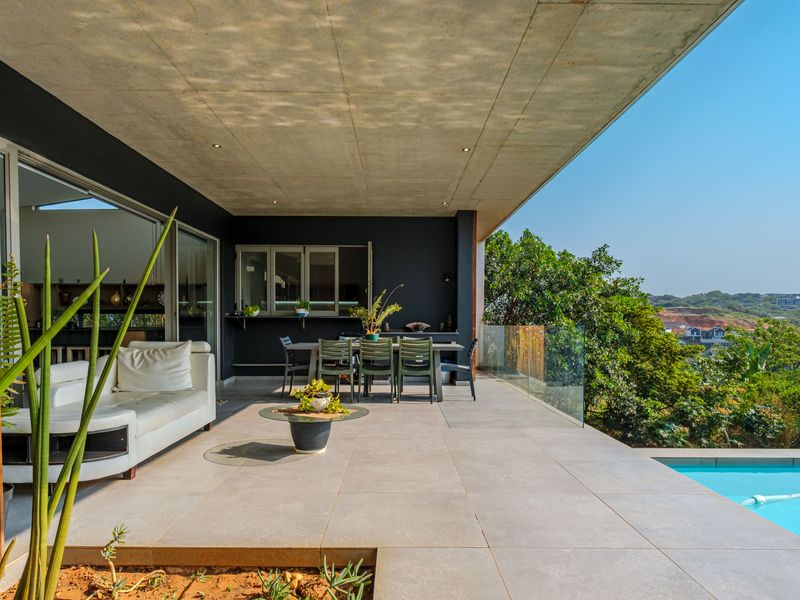 Spacious covered patio featuring modern tiled flooring, a sleek glass balustrade, and direct access to an adjacent swimming pool with scenic views.