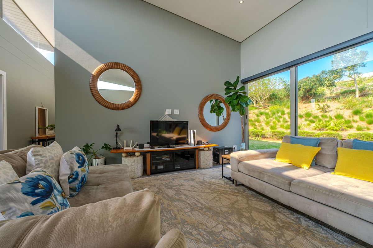 A bright and modern living room featuring high ceilings, recessed lighting, and large sliding glass doors that provide seamless access to the garden.