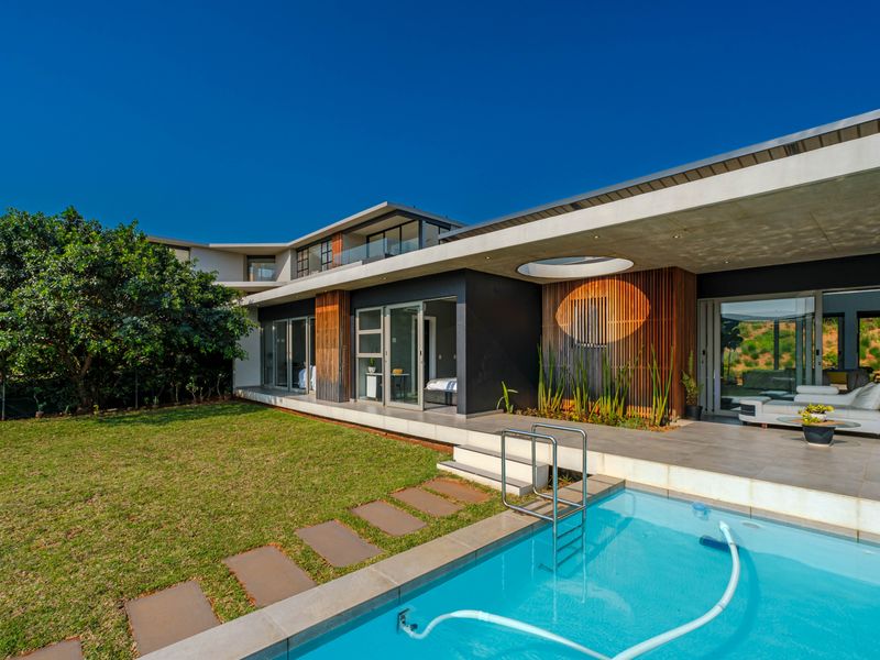 Modern architectural home featuring a swimming pool, expansive concrete patio, and timber-clad facade with seamless indoor-outdoor flow to the garden.