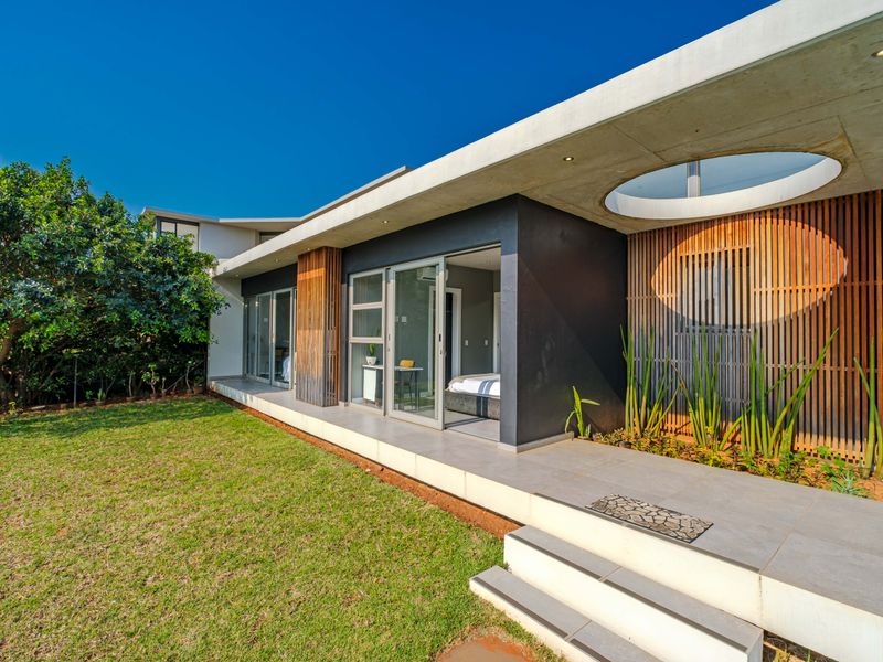 Modern rear exterior featuring a concrete roof overhang with a circular skylight, timber slat detailing, and a tiled patio leading to the garden.