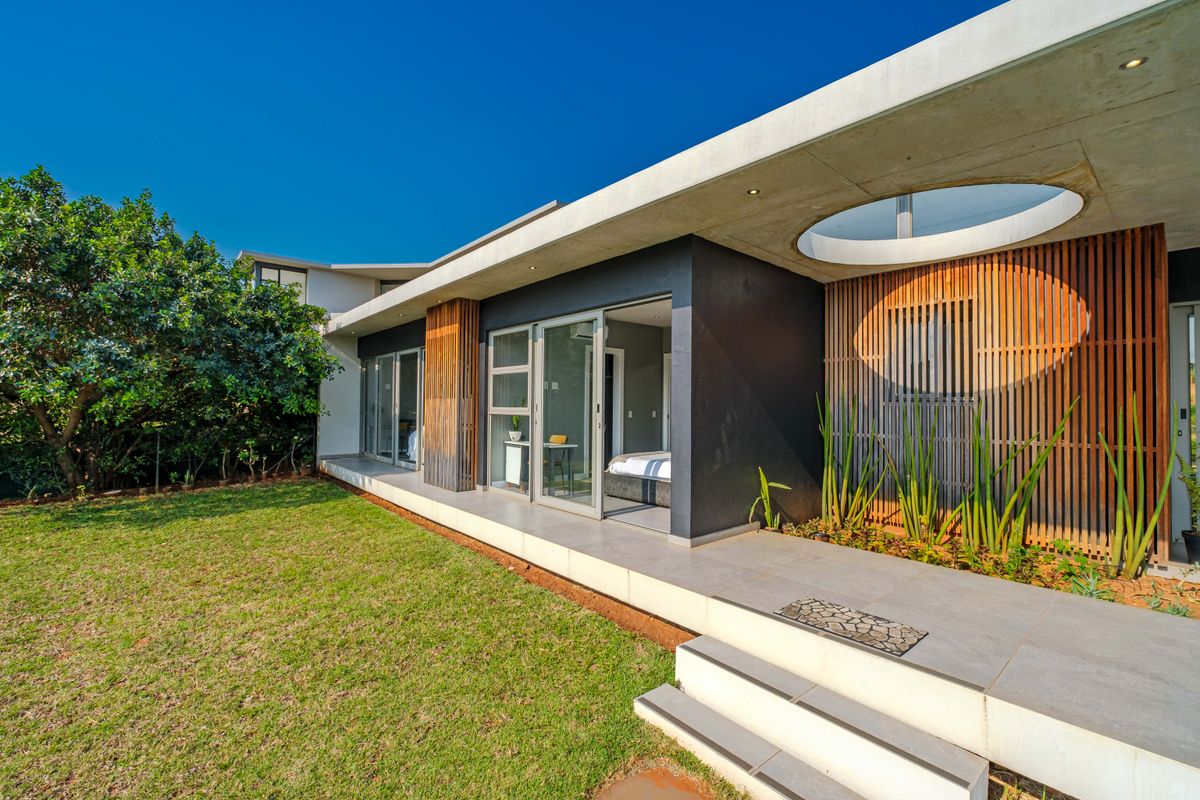 Modern rear exterior featuring a concrete roof overhang with a circular skylight, timber slat detailing, and a tiled patio leading to the garden.