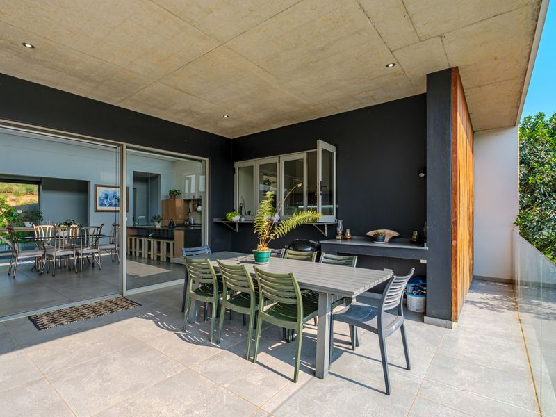 Modern covered patio featuring a concrete ceiling, built-in outdoor counter, and glass balustrade, seamlessly connecting to the indoor living area via large sliding doors.