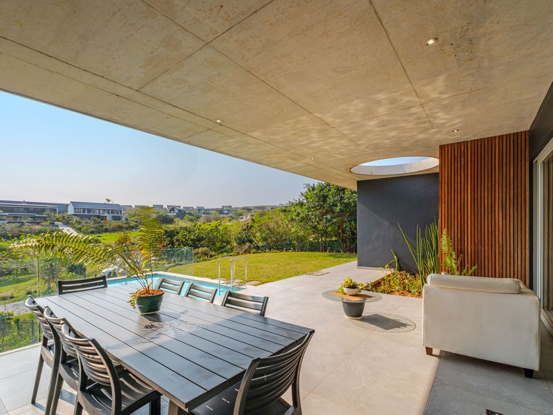 A modern covered patio featuring a concrete ceiling with a circular skylight, timber slat accents, and seamless access to the swimming pool and garden.