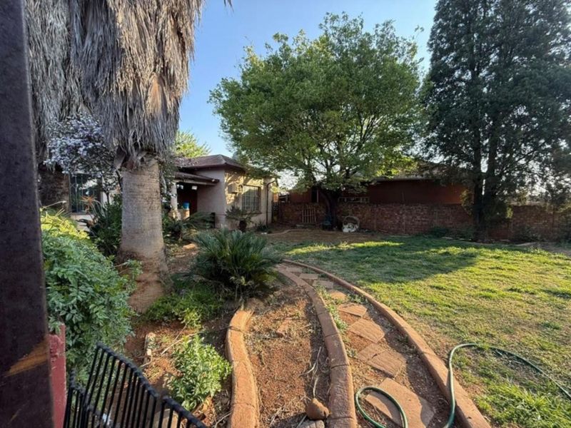 A spacious rear garden featuring a paved pathway, mature trees, and a brick boundary wall, offering potential for landscaping and outdoor living.