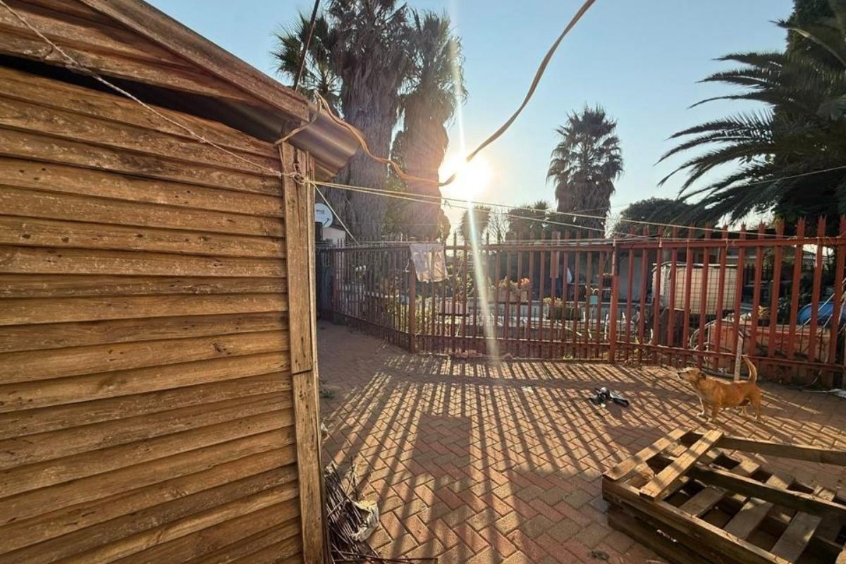 Rear outdoor area featuring a timber-clad structure and paved patio space enclosed by metal perimeter fencing.